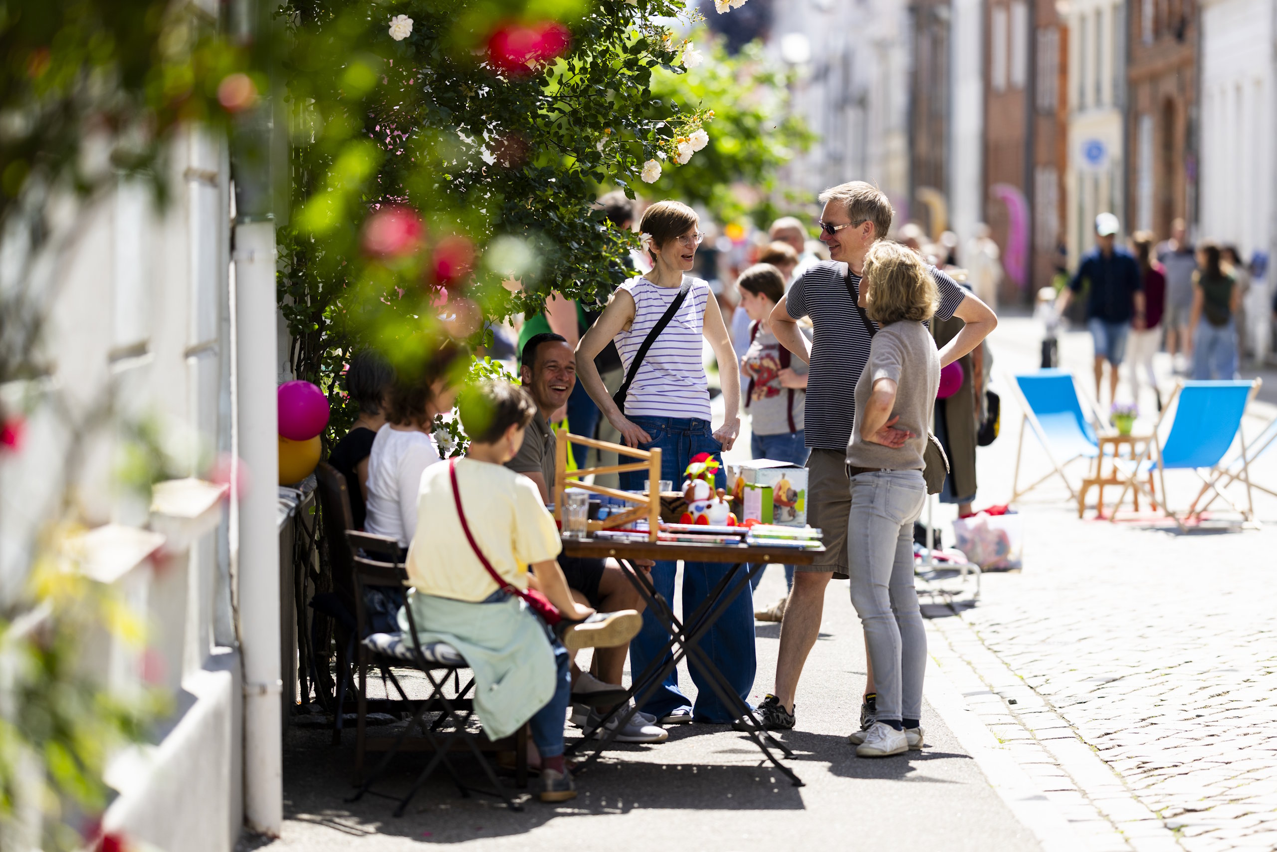 Menschen kommen an einem Straßenfest mit Sitzgelegenheiten und Blumenschmuck in der Lübecker Altstadt zusammen.
