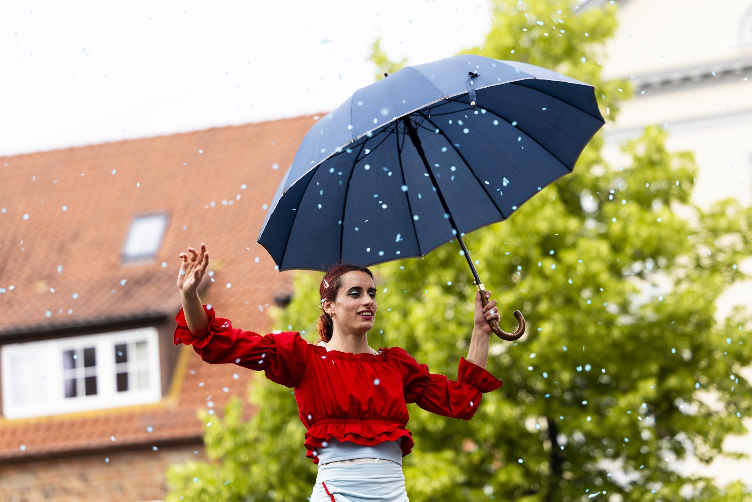 Artistin mit blauem Regenschirm und roter Bluse tritt beim HanseKulturFestival in Lübeck auf.