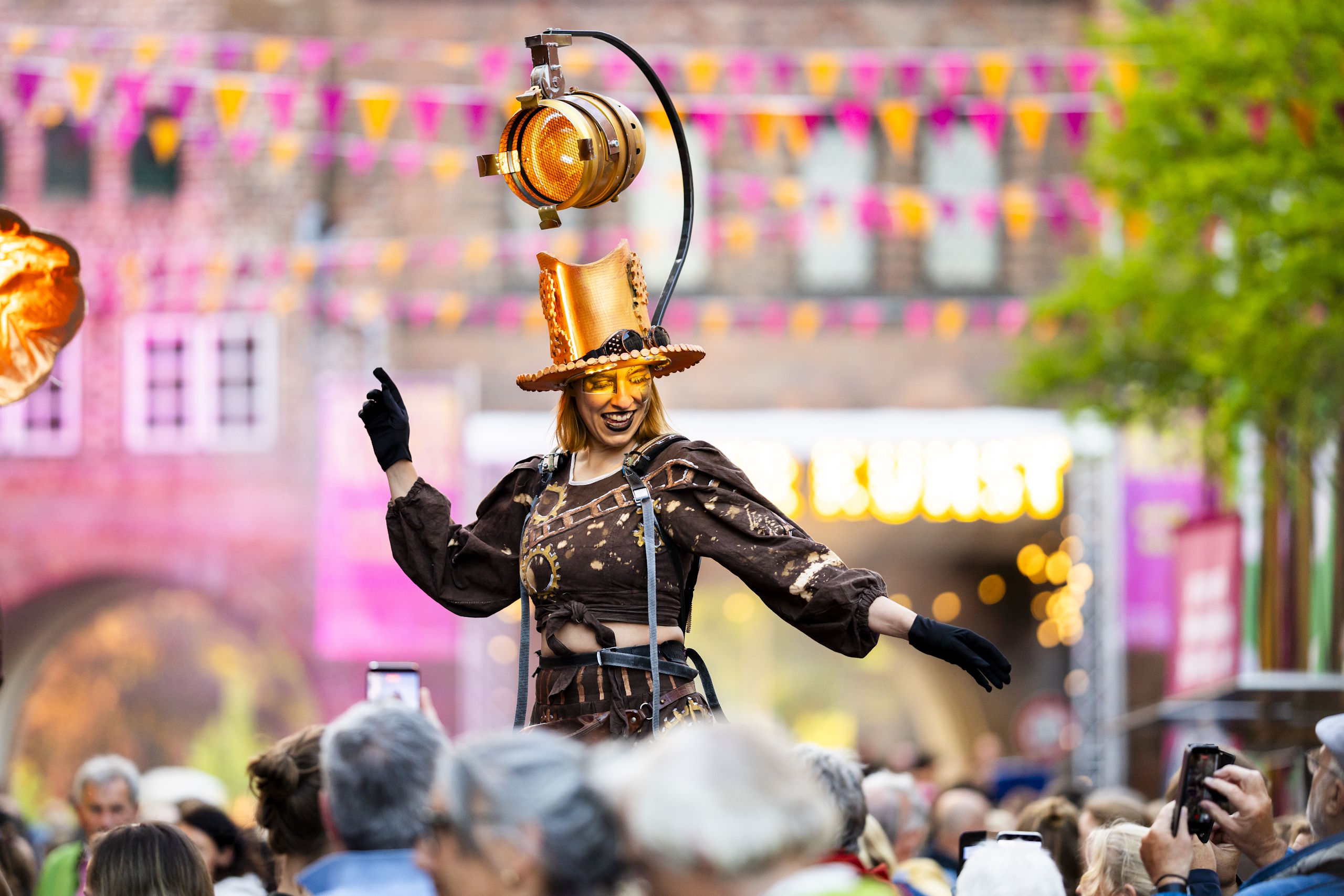 Stelzenkünstlerin mit beleuchtetem Hut und goldenem Make-up vor Festivalpublikum in Lübeck.