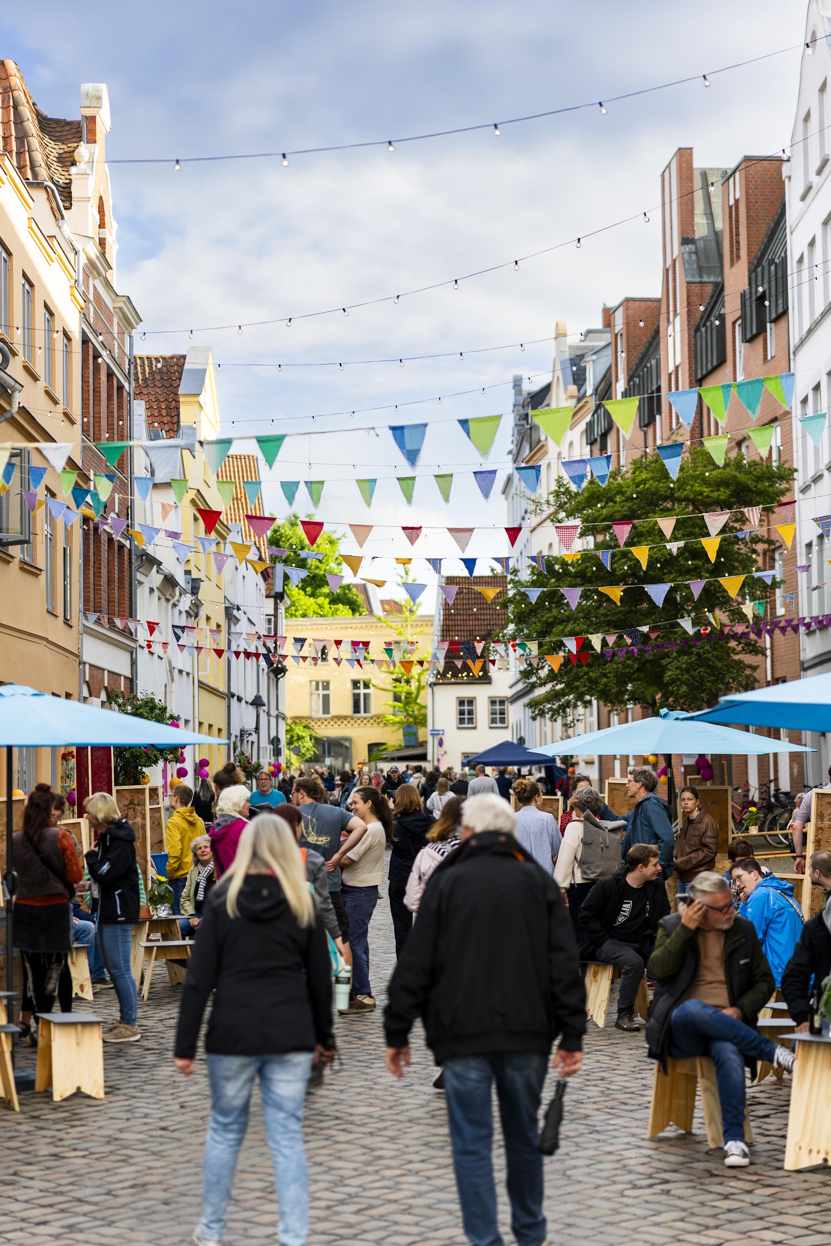 Besucherinnen und Besucher genießen das Straßenfest in einer mit Wimpelketten geschmückten Altstadtgasse.