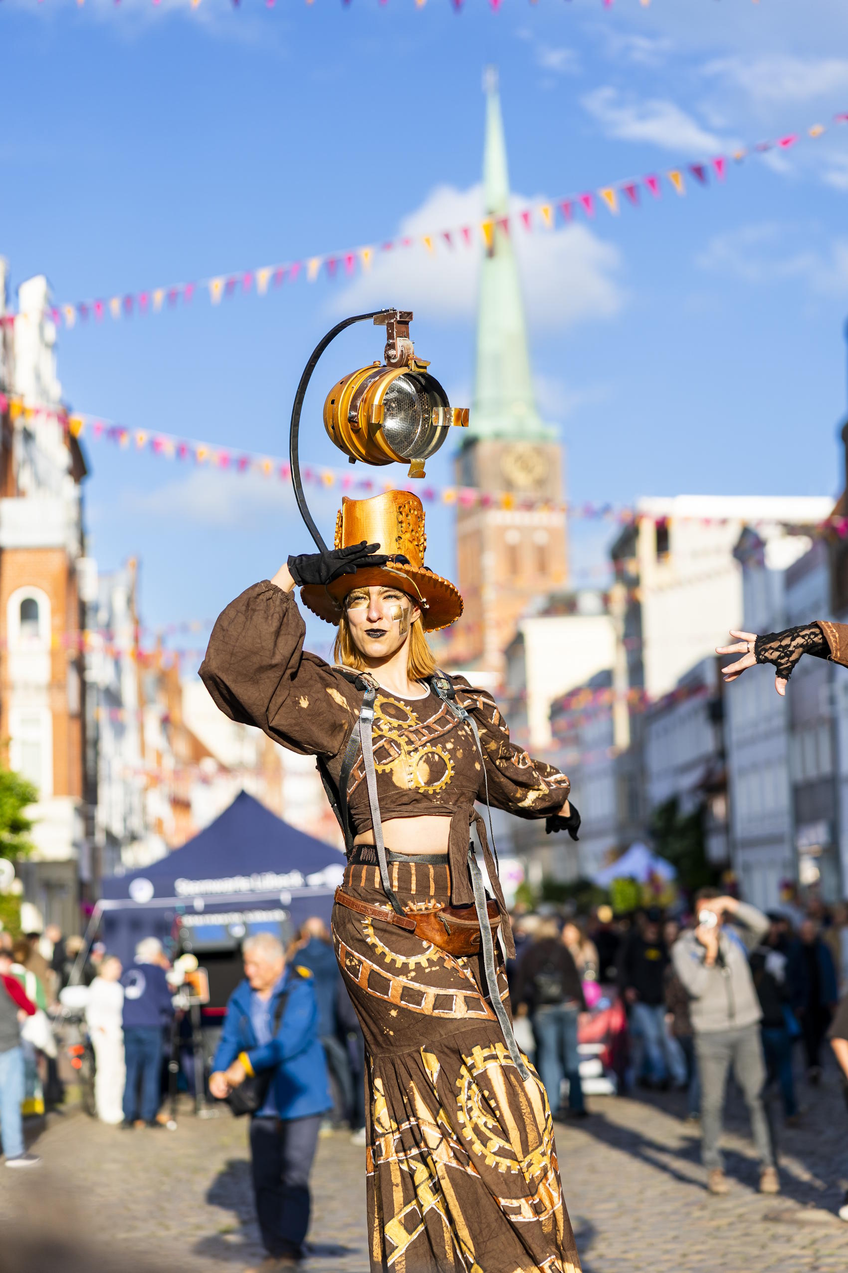 Stelzenkünstlerin im Steampunk-Kostüm vor Publikum in der festlich geschmückten Lübecker Altstadt.