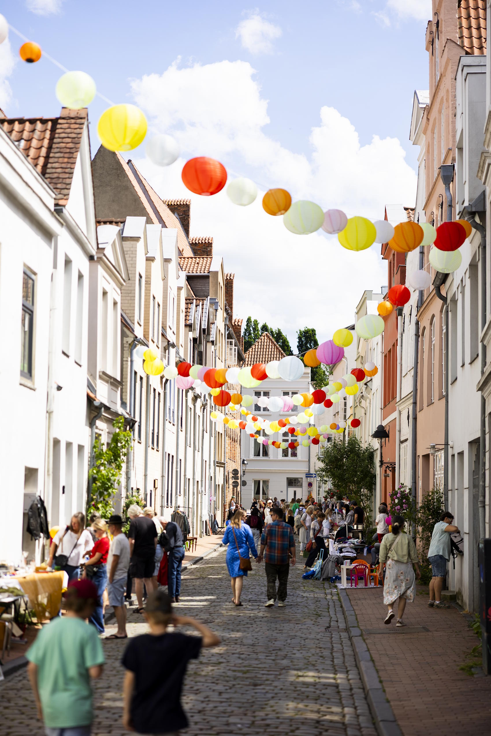Besucherinnen und Besucher flanieren durch eine mit bunten Lampions dekorierte Altstadtstraße in Lübeck.
